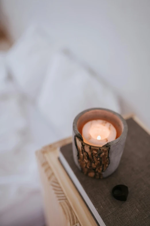 a candle that is sitting on top of a book, a marble sculpture, trending on pexels, bed, light haze, holding a burning wood piece, looking towards camera