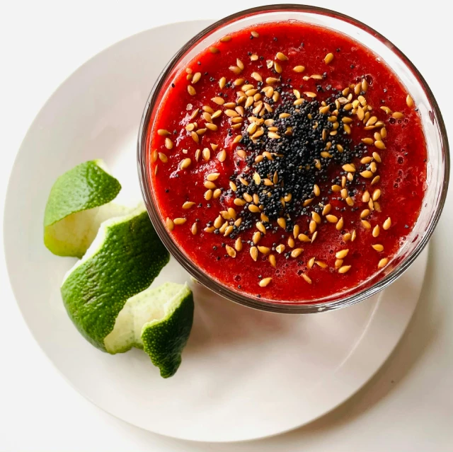 a white plate topped with a bowl of soup next to a lime, blood red, seeds, slush, detailed product image