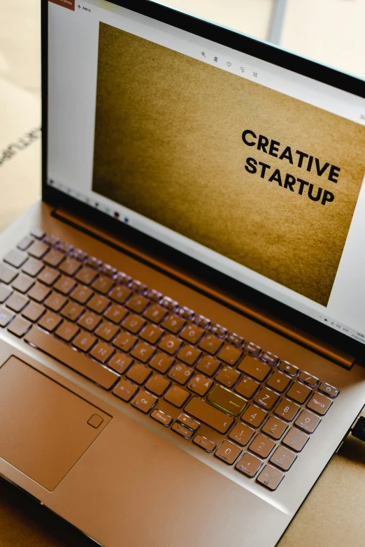 a laptop computer sitting on top of a wooden table, by Byron Galvez, trending on pexels, computer art, lettering, ai startup, indi creates, gold