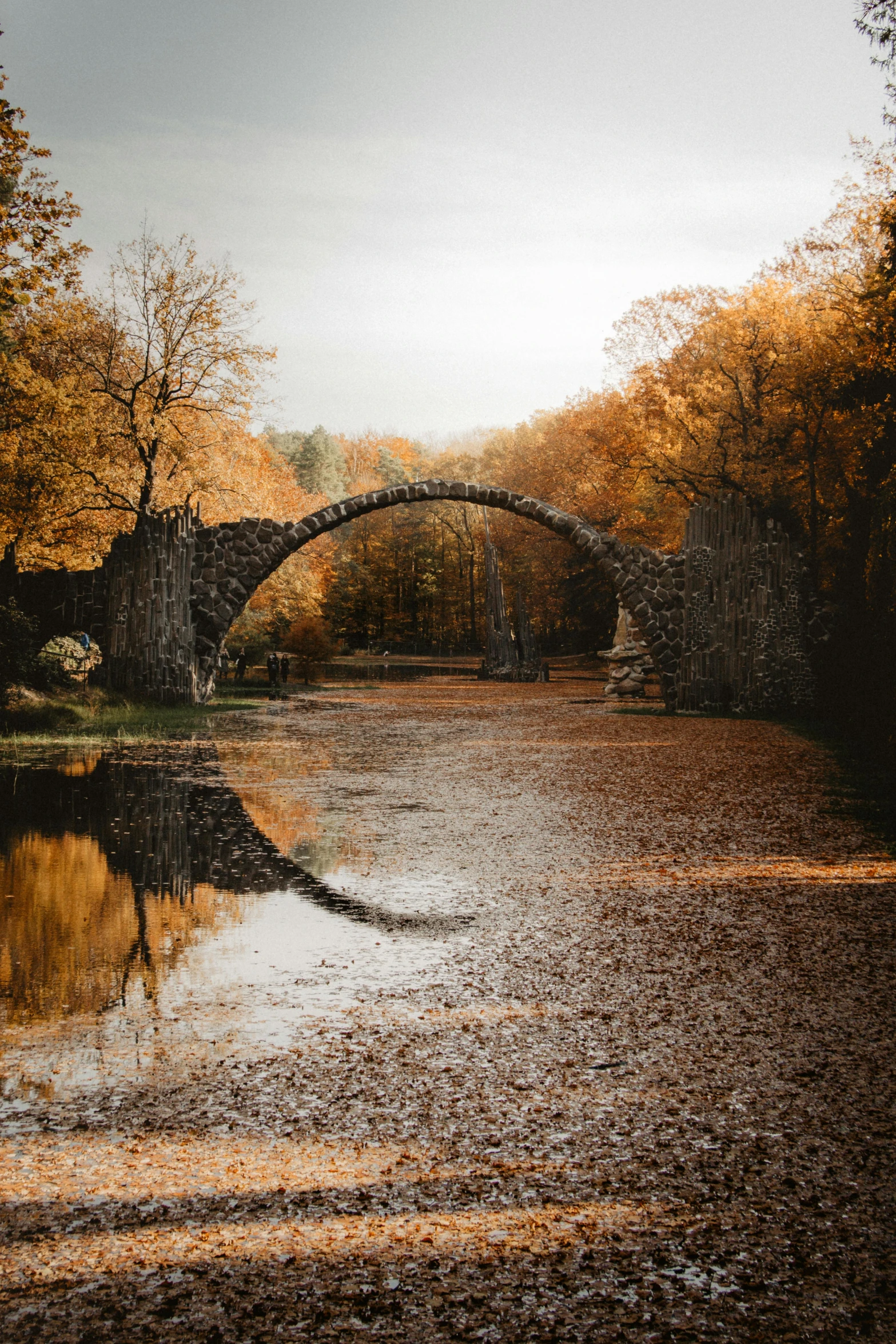 a bridge over a body of water surrounded by trees, by Sebastian Spreng, pexels contest winner, romanticism, stone walls, 🍂 cute, massive arch, 4 k cinematic photo