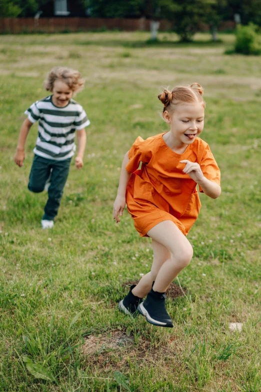 a couple of kids running across a lush green field, wearing an orange t shirt, wearing track and field suit, premium quality, playing games