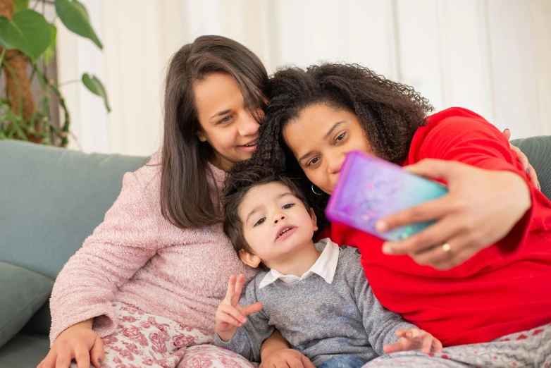 a group of women sitting on top of a couch, a picture, pexels, happening, portrait of family of three, she is holding a smartphone, purple, multicoloured