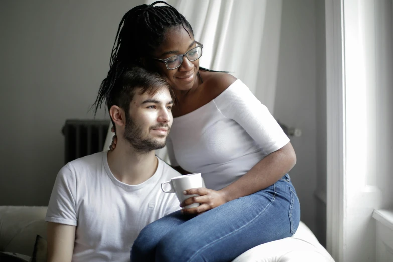 a man and a woman sitting on a couch, a photo, trending on pexels, lgbt, white mug, ( ( dark skin ) ), looking her shoulder