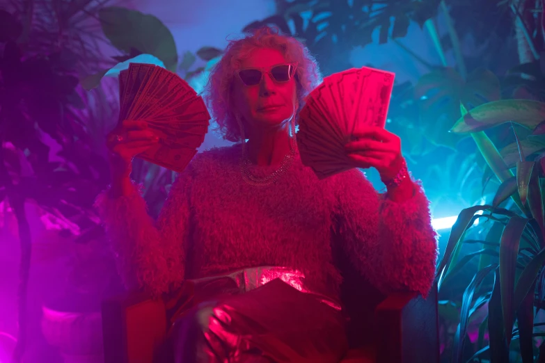 a woman sitting in a chair holding a fan, an album cover, inspired by Elsa Bleda, pexels contest winner, maximalism, leaves as dollars!! glow, elderly woman, vaporwave lights, scene from fightclub movie