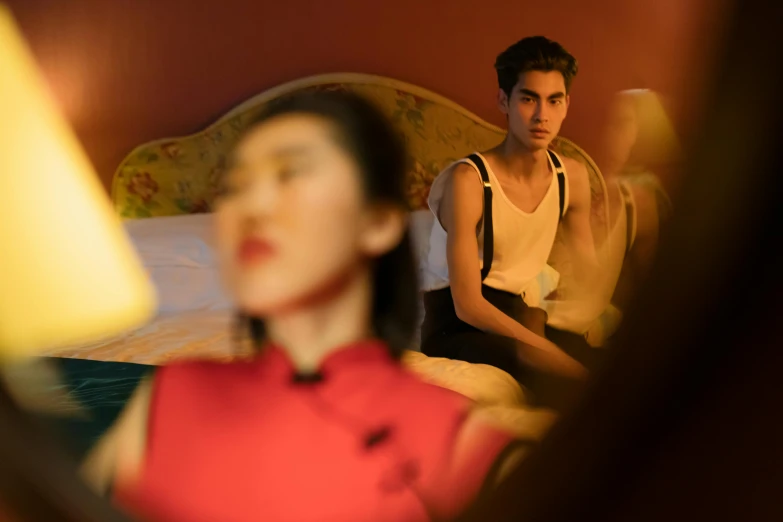 a woman sitting on top of a bed next to a man, inspired by Nan Goldin, trending on pexels, surrealism, cai xukun, red cloth around his shoulders, looking into a mirror, promotional image