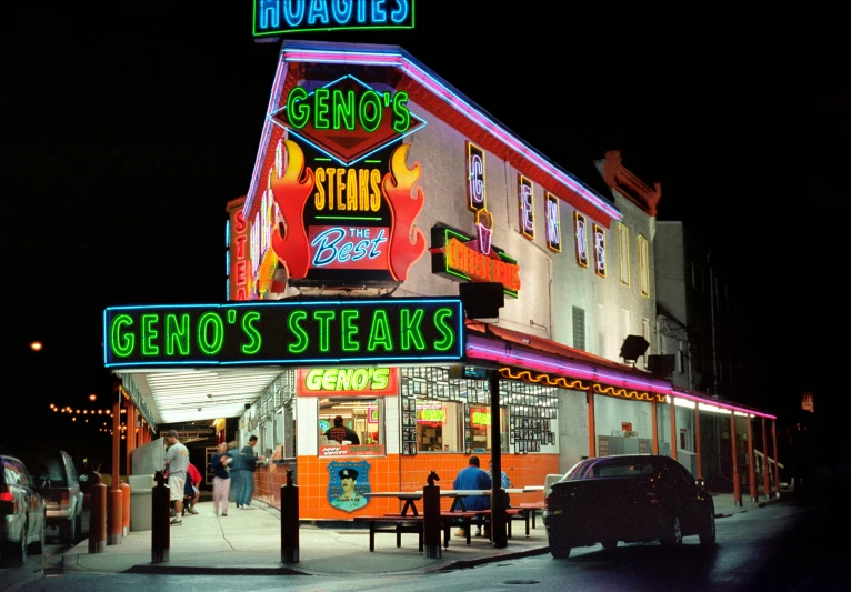 a neon sign that says geno's steaks on the side of a building, by Glen Angus, pexels, photorealism, 1980s photo, taverns nighttime lifestyle, a brightly coloured, getty images