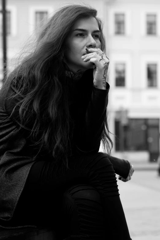 a black and white photo of a woman sitting on a bench, pexels contest winner, antipodeans, messy long black hair, smoking outside, in london, hand on her chin