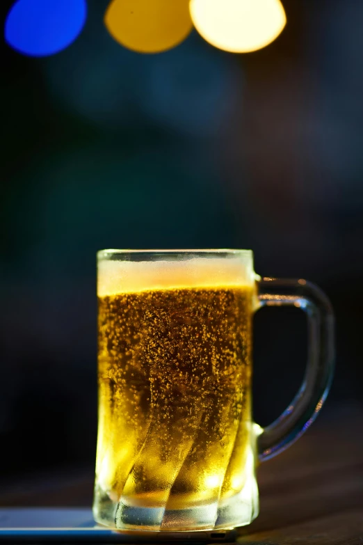 a glass of beer sitting on top of a wooden table, by Jason Felix, pexels, gold and green, during the night, bokeh soft, blue