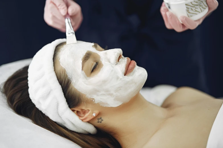 a woman getting a facial mask at a spa, by Julia Pishtar, trending on pexels, art nouveau, white, rectangle, beaten, porcelain skin ”