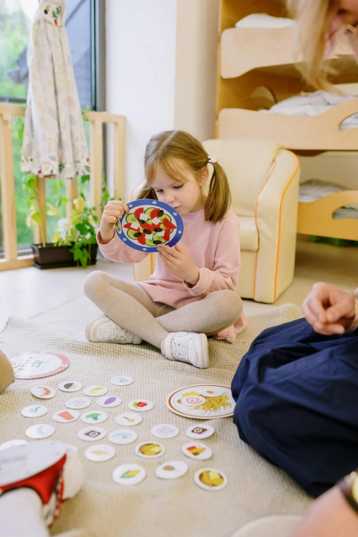 a group of people sitting on the floor playing a game, children playing with pogs, offering a plate of food, profile image, thumbnail