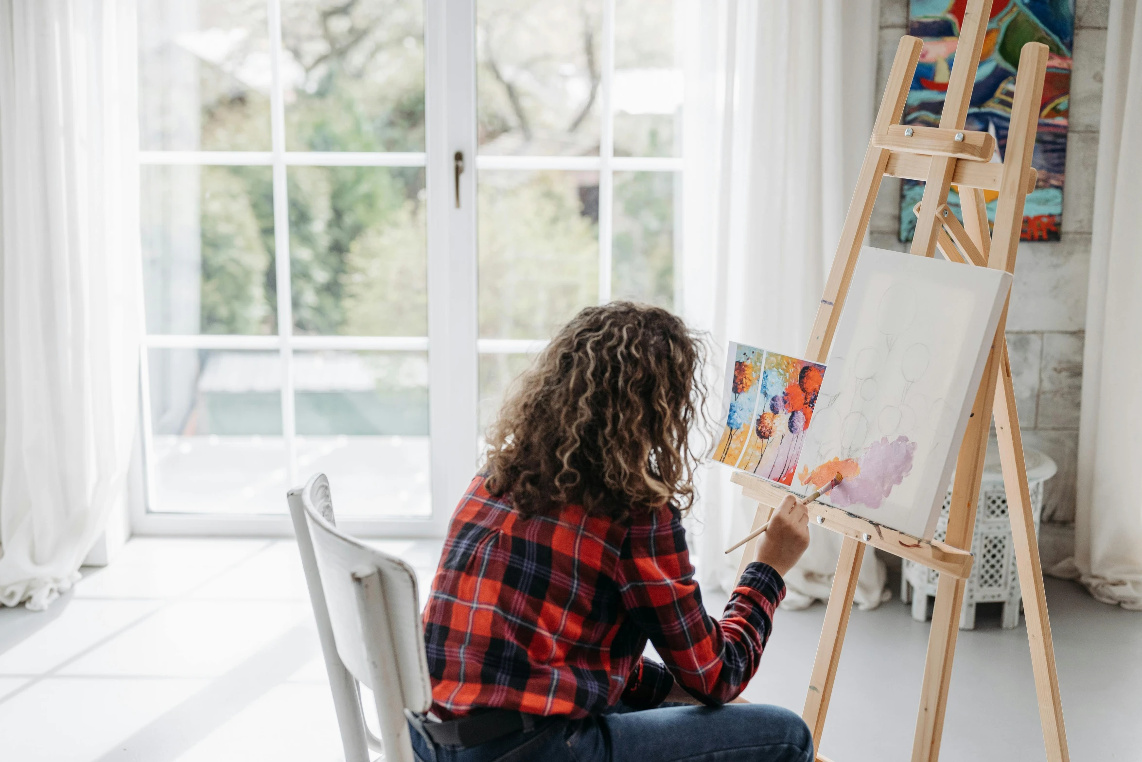 a woman sitting on a chair in front of a painting easel, pexels contest winner, next to window, trending on artlist, on a white table, painting a canvas