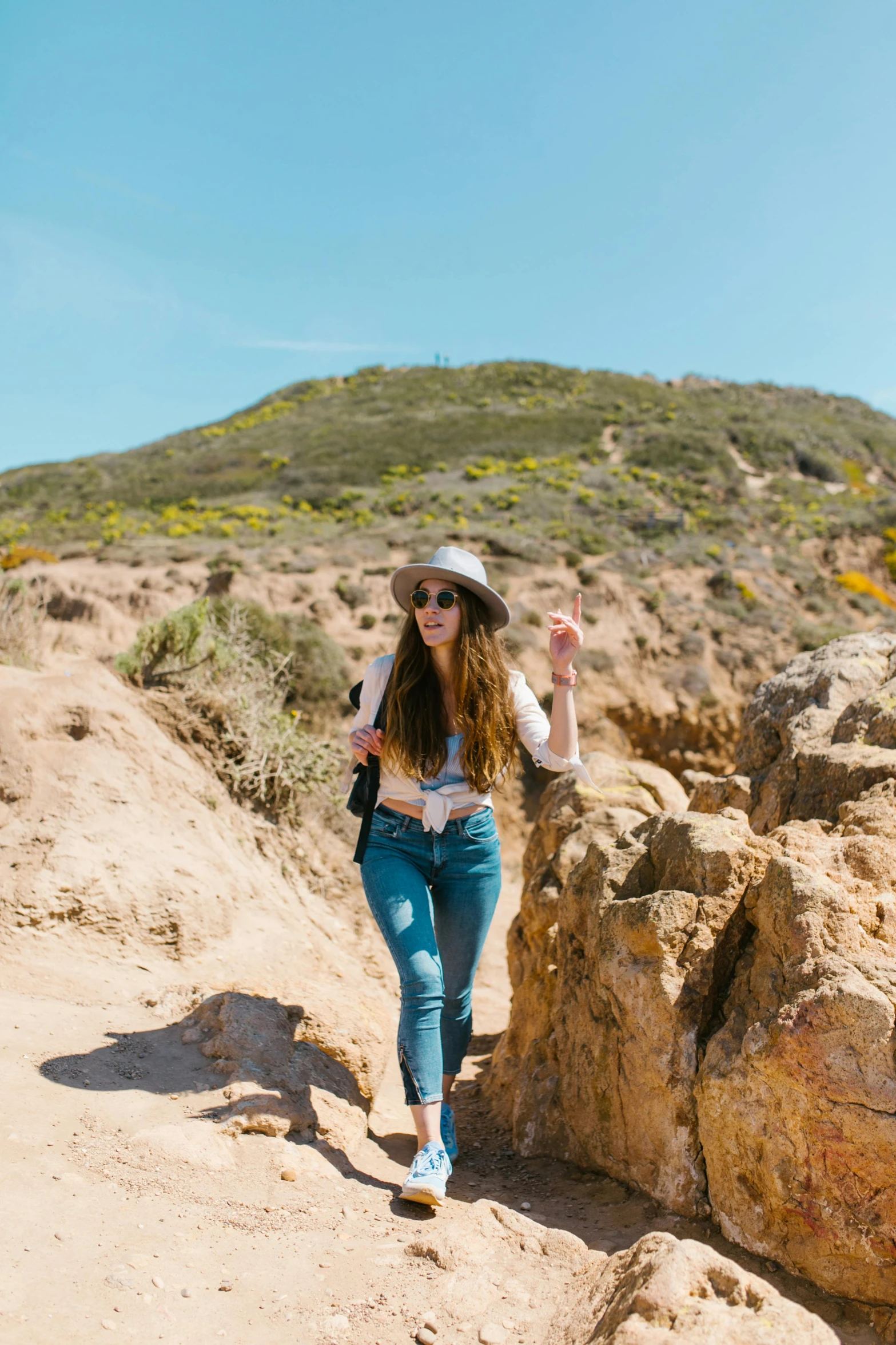 a woman standing on top of a rocky hill, by Whitney Sherman, trending on unsplash, hollister ranch, bright sunny day, walking on the sand, standing in a grotto