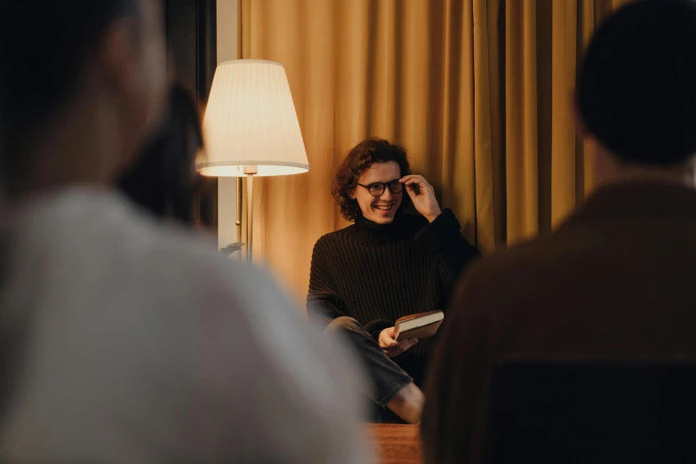 a man sitting in a chair talking on a cell phone, by Emma Andijewska, pexels contest winner, girl with glasses, hygge, group photo, holding a book