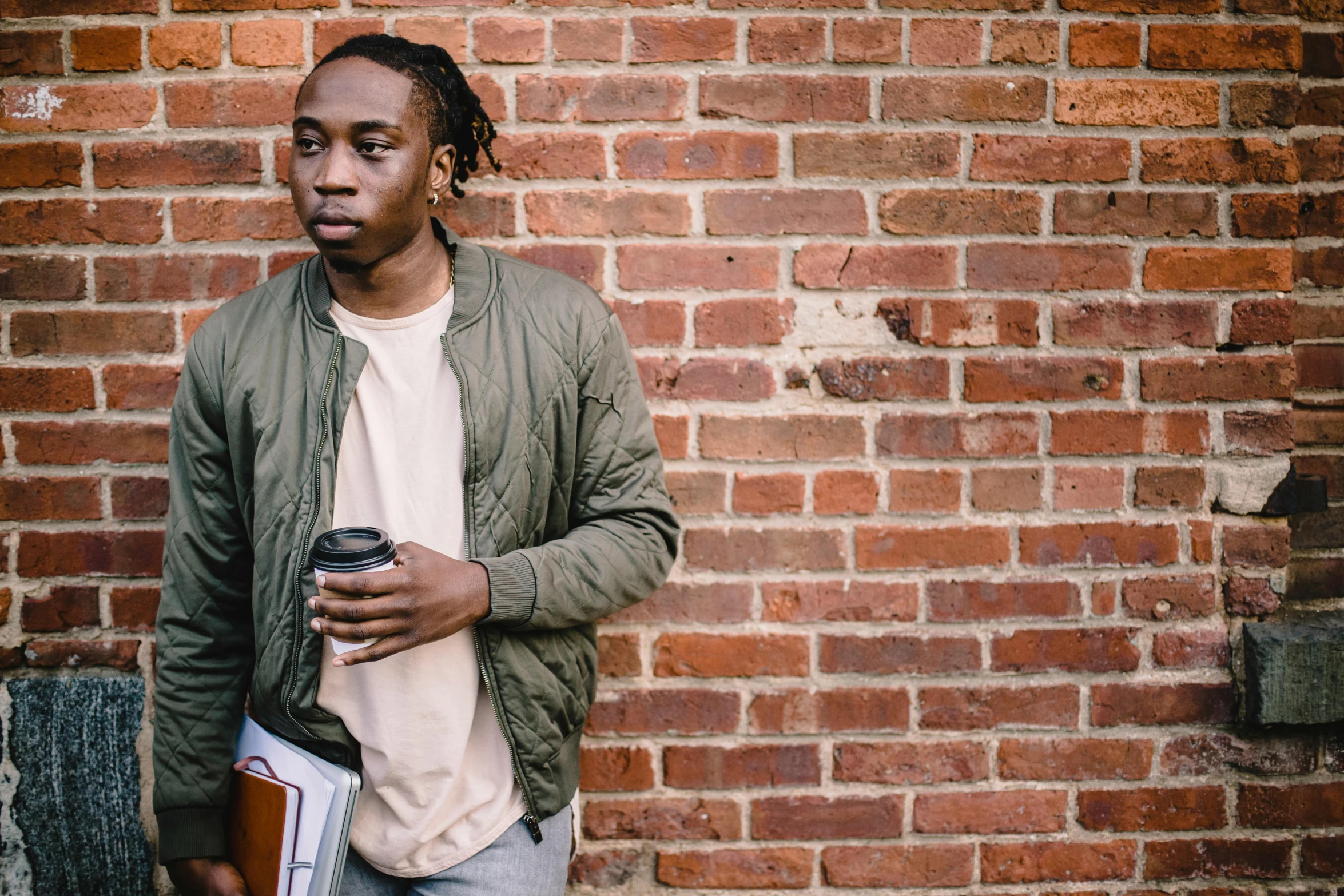 a man standing in front of a brick wall, by Stokely Webster, trending on unsplash, wiz khalifa, with brown skin, student, looking distracted