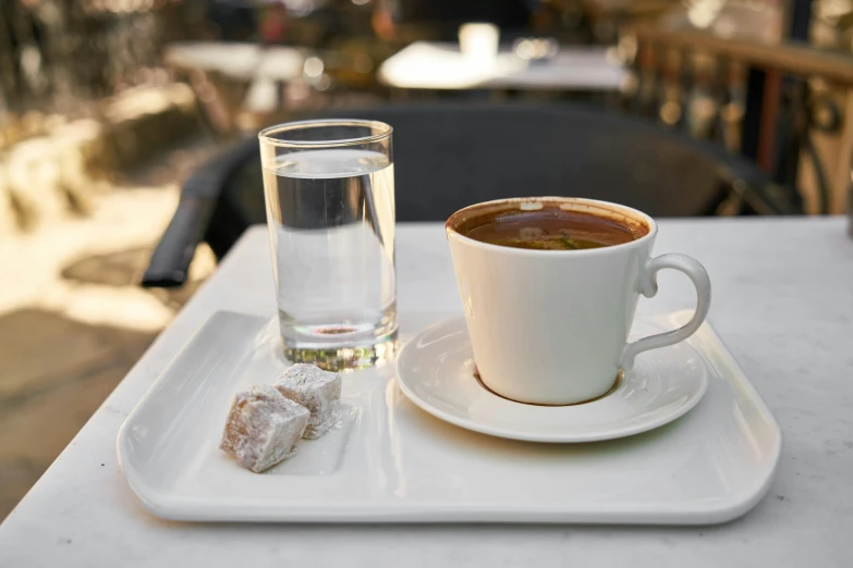 a cup of coffee on a tray next to a glass of water, inspired by Constantine Andreou, hurufiyya, cafe, grey, square, turkey