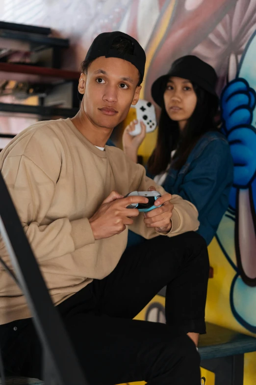 a man and a woman sitting next to each other, graffiti, holding a nintendo switch, he is wearing a brown sweater, lee madgwick & liam wong, portrait image