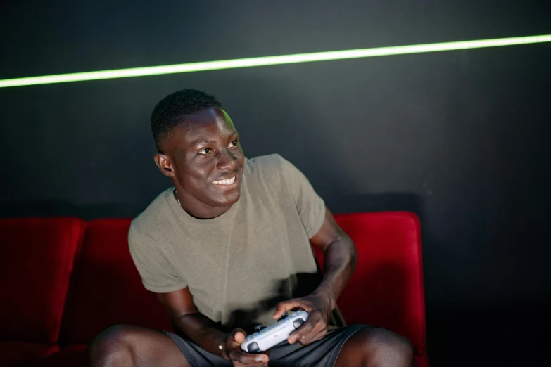 a man sitting on a red couch holding a video game controller, inspired by David Bailly, pexels contest winner, happening, grey skinned, green ambient light, avatar image, soccer