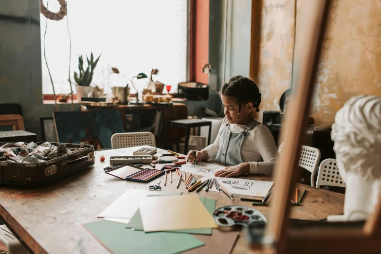 a woman sitting at a table working on a piece of art, a child's drawing, pexels contest winner, girl in studio, in a workshop, avatar image, high quality artwork