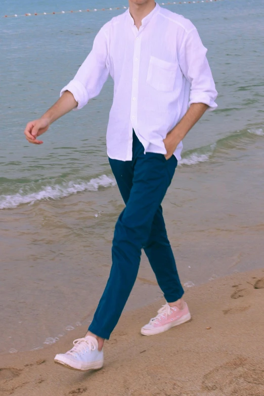 a man walking on a beach next to the ocean, blue pants, wearing a white button up shirt, coloured, cords