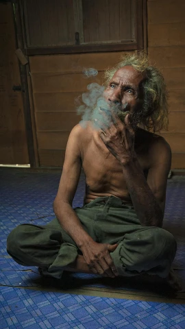 a man sitting on the floor smoking a cigarette, pexels contest winner, sumatraism, a photo of a disheveled man, hemp, south east asian with long, indistinct man with his hand up