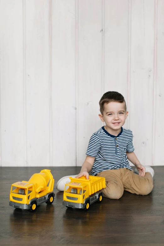 a little boy sitting on the floor playing with construction vehicles, inspired by Sam Havadtoy, grey, product display photograph, yellow, small