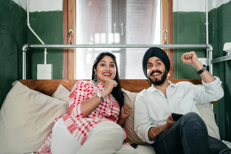 a man and a woman sitting on a bed, inspired by Manjit Bawa, pexels contest winner, sitting on a couch, square, watching tv, both smiling for the camera