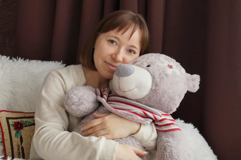 a woman sitting on a bed holding a teddy bear, by Julia Pishtar, pexels contest winner, hugging each other, russian girlfriend, avatar image, grey
