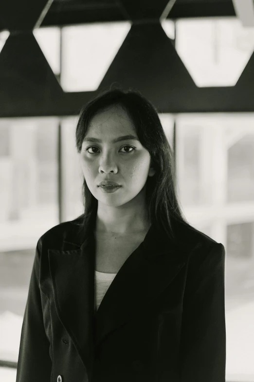 a black and white photo of a woman standing in front of a window, inspired by Ruth Jên, a man wearing a black jacket, malaysian, serious look, architect