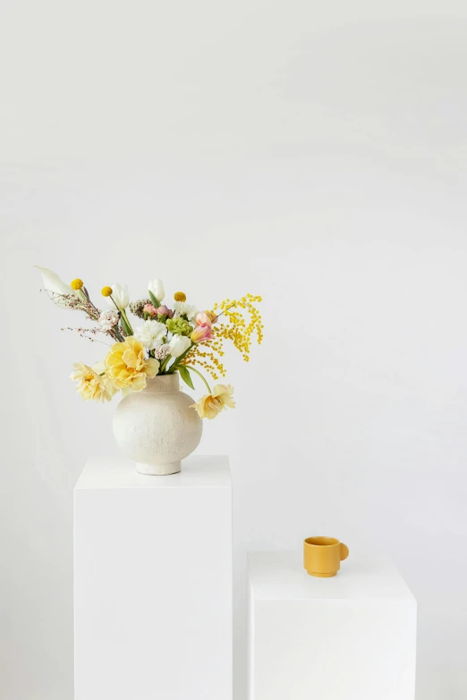 a white vase sitting on top of a white pedestal, a still life, by Liza Donnelly, trending on unsplash, yellow scheme, in a white boho style studio, soft flowers, snacks