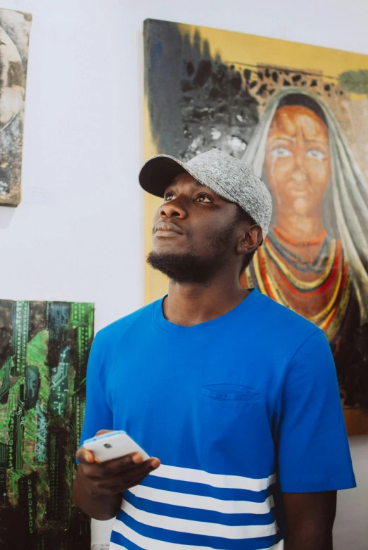 a man standing in front of a bunch of paintings, an album cover, by Chinwe Chukwuogo-Roy, pexels contest winner, looking away from camera, looking at his phone, slightly smiling, avatar image