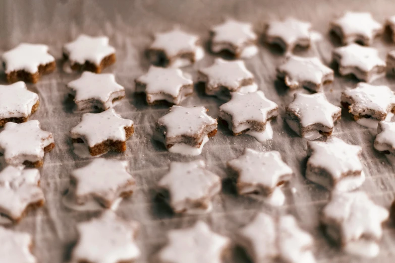 a table topped with lots of cookies covered in icing, a tilt shift photo, by Emma Andijewska, pexels, lots of stars, made out of shiny white metal, background image, recipe