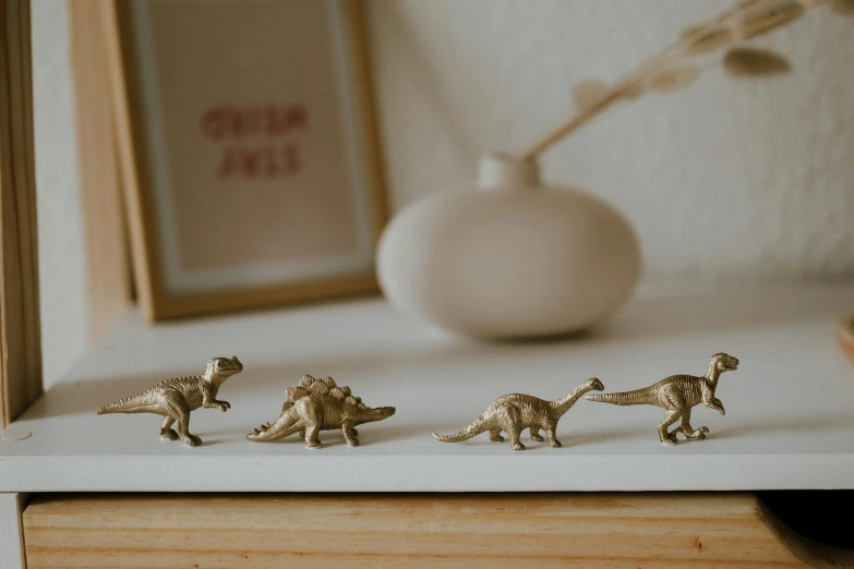 a couple of figurines sitting on top of a table, a macro photograph, trending on unsplash, chrome dino, gold decoration, in a row, product introduction photo