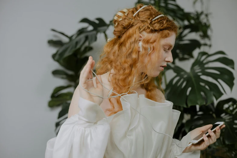 a woman in a white dress holding a cell phone, an album cover, inspired by Alexandre Cabanel, trending on pexels, pre-raphaelitism, hair are curled wired cables, ginger wavy hair, practical effects, with head phones