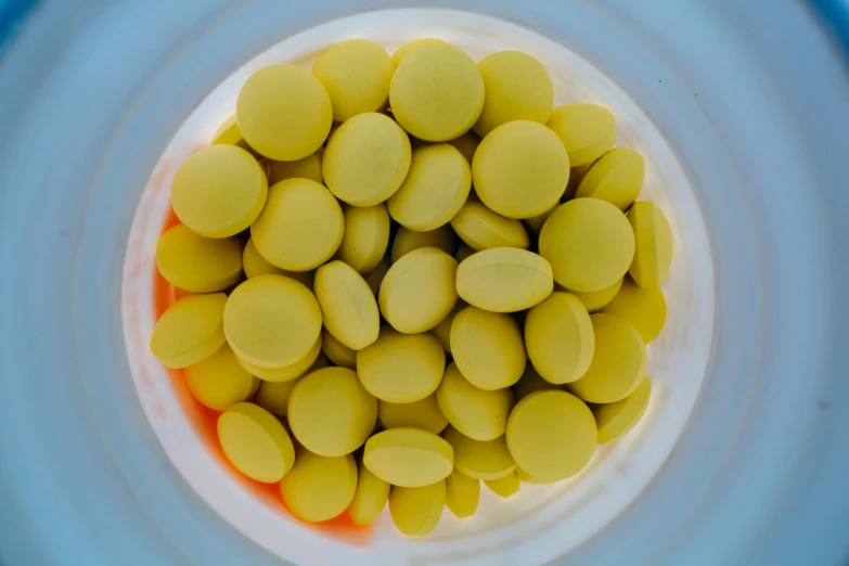 a white bowl filled with yellow beans on top of a blue table, a picture, pexels, antipodeans, pills, algae, futuristic yellow lens, thumbnail