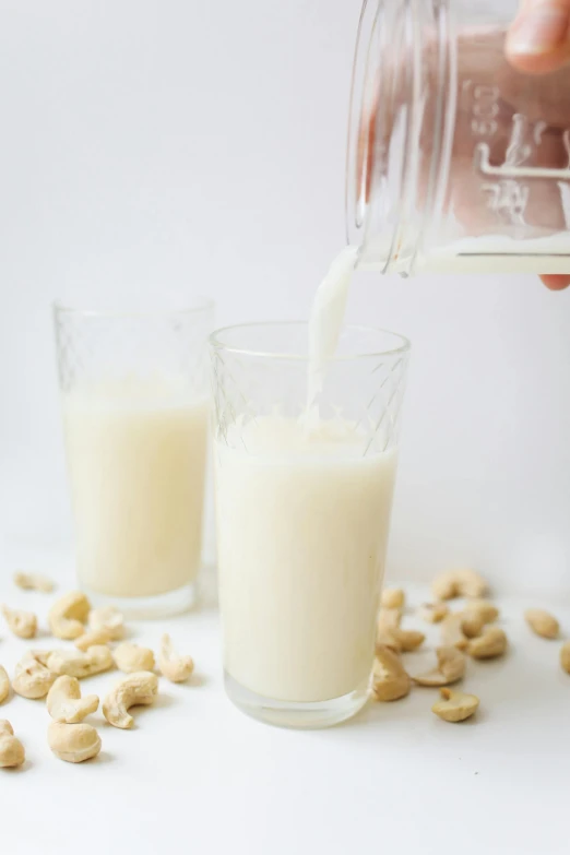 a person pouring milk into a glass filled with cashews, thumbnail, white bg, drink milkshakes together, shiny and sparkling