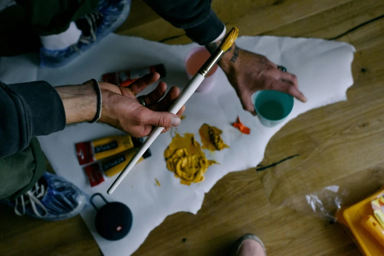 a couple of people sitting on top of a wooden floor, a hyperrealistic painting, pexels contest winner, holding a paintbrush in his hand, paper marbling, yellow ochre, holding a wooden staff