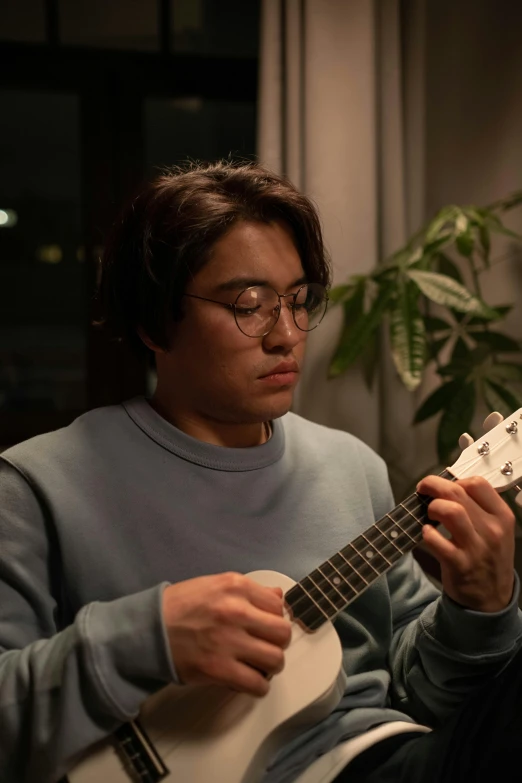 a man sitting on a couch playing a guitar, an album cover, inspired by Reuben Tam, reddit, ukulele, shot with sony alpha, in a japanese apartment, headshot