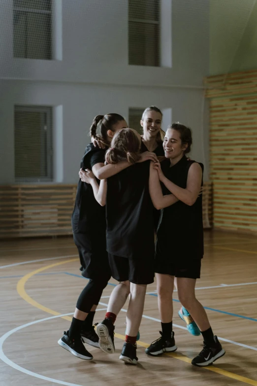 a group of people standing on top of a basketball court, by Attila Meszlenyi, danube school, hugging each other, indoor shot, young women, performance