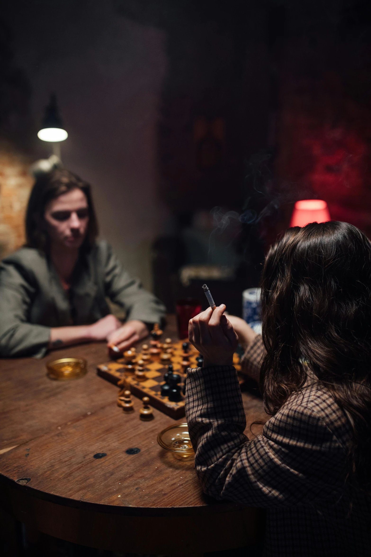 two people sitting at a table playing chess, inspired by Elsa Bleda, cozy dark 1920s speakeasy bar, dafne keen, 2019 trending photo, smoking