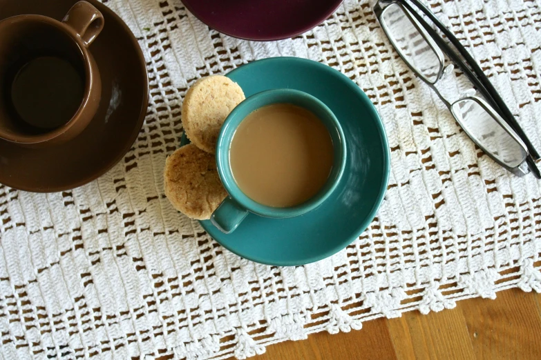 a cup of coffee and some cookies on a table, a portrait, inspired by Richmond Barthé, unsplash, dau-al-set, teal, beige, medium-shot, colorful”