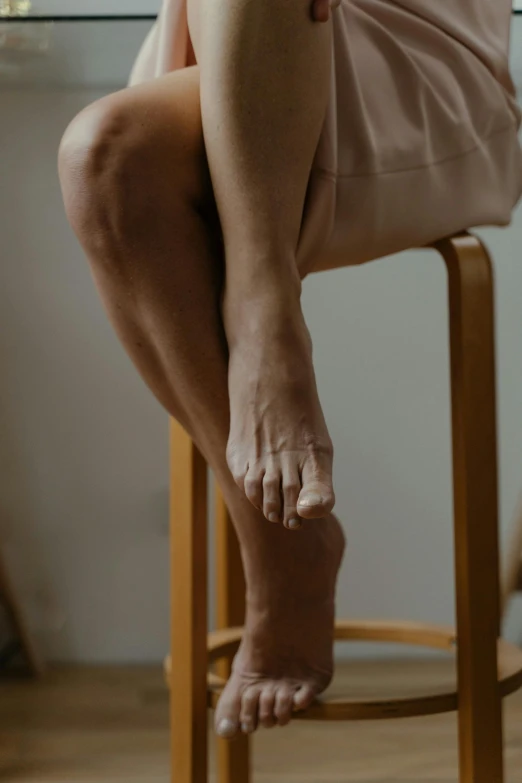 a woman sitting on top of a wooden stool, trending on pexels, hyperrealism, veins merged feet head, tendons, blurred, compassionate