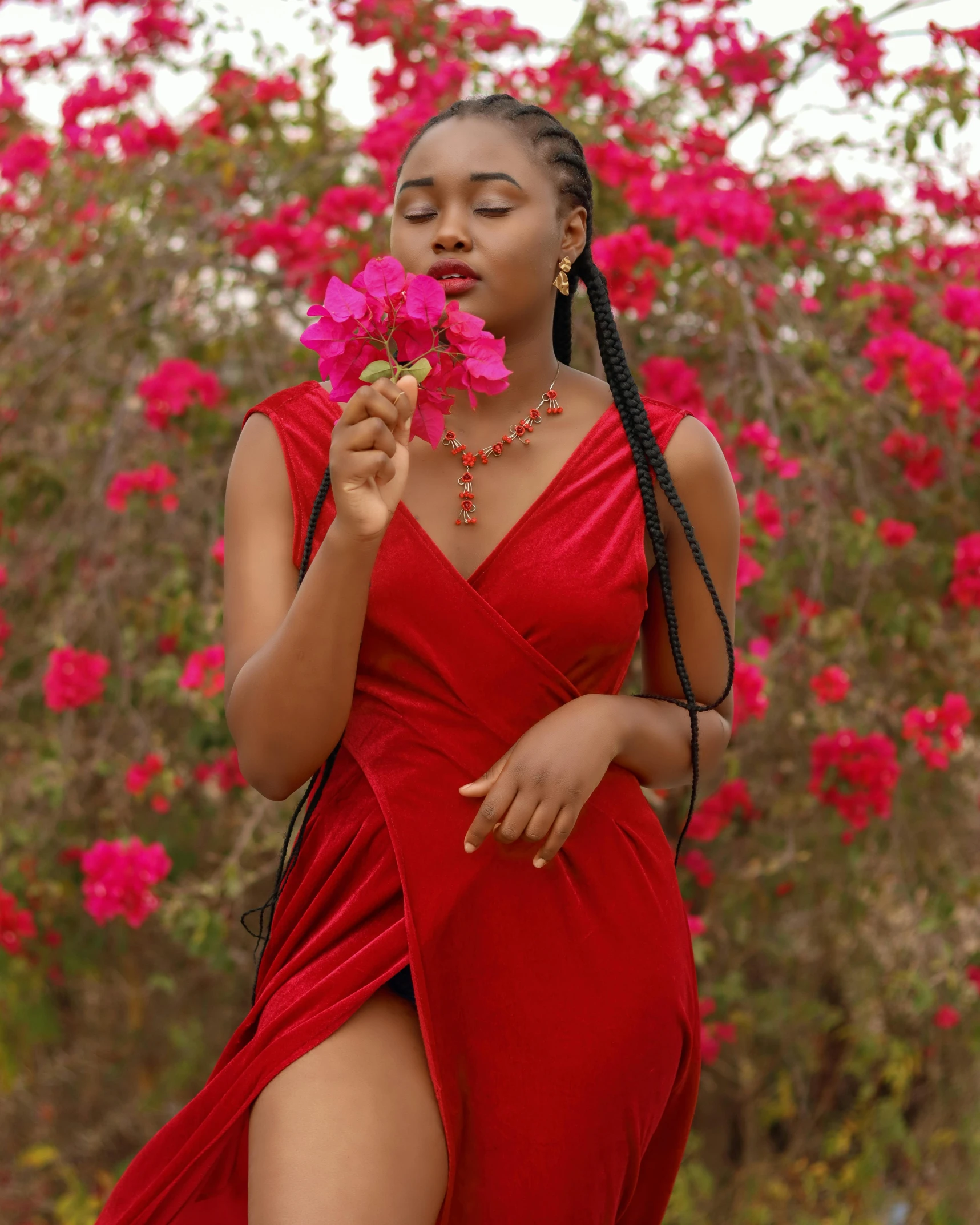 a woman in a red dress holding a flower, by Chinwe Chukwuogo-Roy, pexels contest winner, smooth red skin, bougainvillea, black teenage girl, corals are gemstones