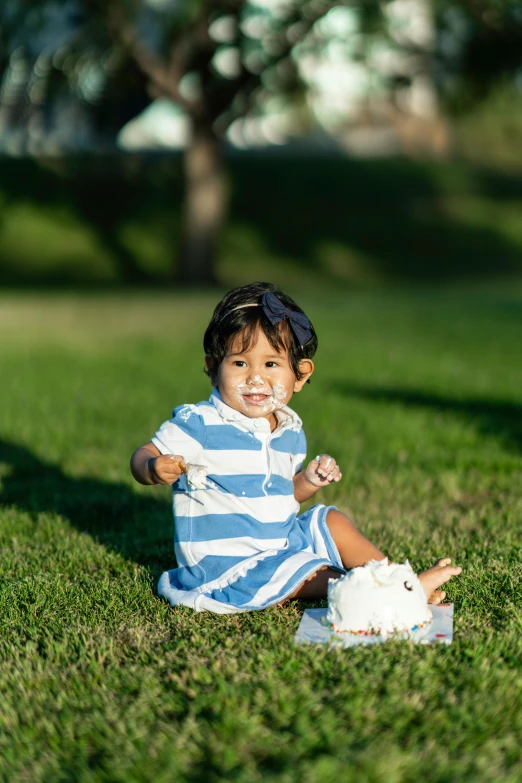 a small child sitting on top of a lush green field, holding a birthday cake, at a park, profile image