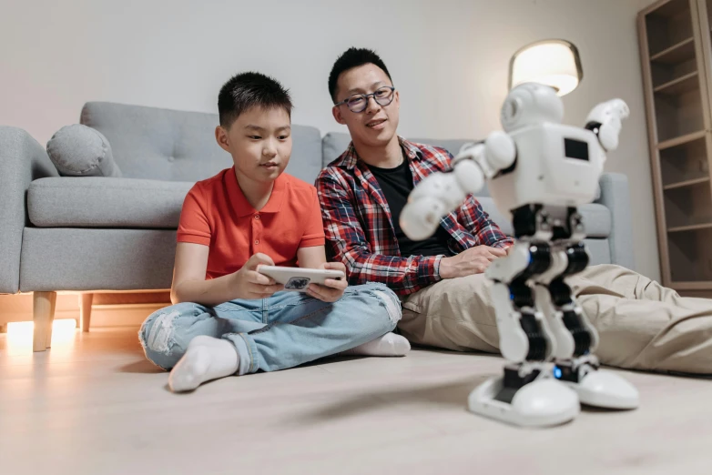 a man and a boy sitting on the floor next to a robot, pexels contest winner, ross tan, parents watching, avatar image, teaching