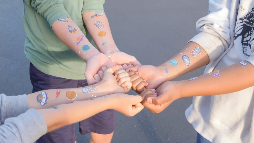 a group of people putting their hands together, a tattoo, solar punk product photo, for kids, covered solar system, multicoloured