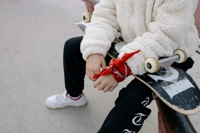 a person sitting on a bench with a skateboard, by Emma Andijewska, trending on pexels, red bandana, white scarf, high details on clothes, wearing a track suit