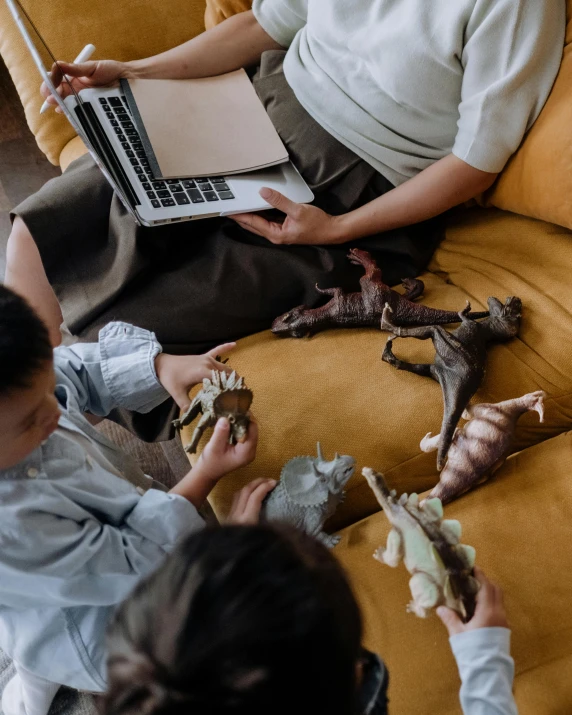 a group of people sitting on a couch with a laptop, inspired by Maurice Sendak, pexels contest winner, dinosaur bones, children's toy, treasures, triceratops