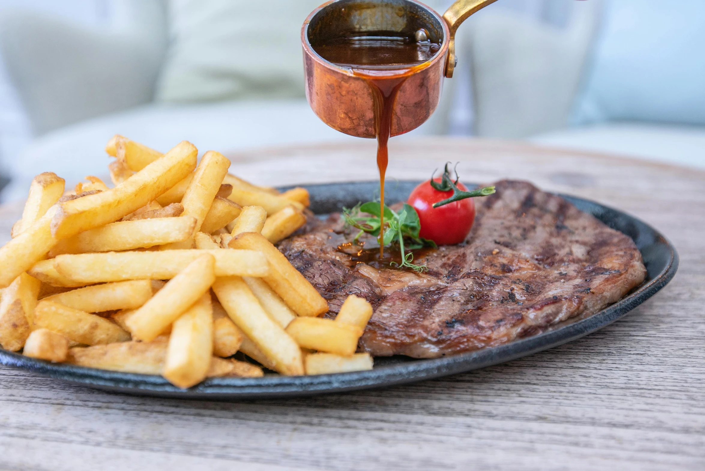 a close up of a plate of food with fries, by Julia Pishtar, steak, brown sauce, bronze, at the waterside