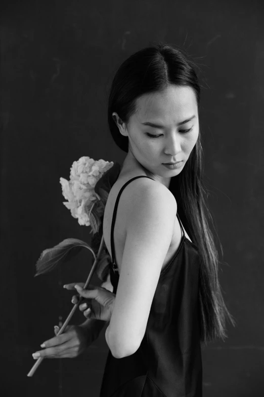 a black and white photo of a woman holding a flower, inspired by Zhang Shuqi, long thin black hair, jen yoon, her hand is on her waist, looking her shoulder