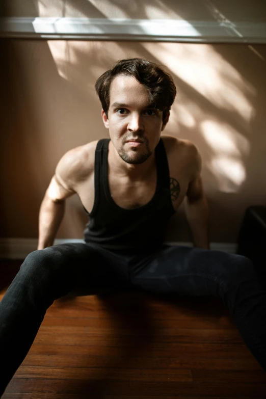 a man sitting on top of a wooden floor, an album cover, by Jessie Alexandra Dick, wearing a tanktop, intense expression, lgbtq, charlie cox